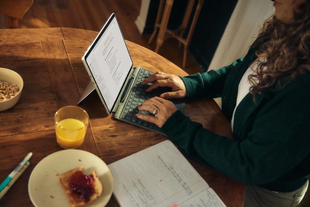 Person typing on a laptop at a wooden table with notes beside them